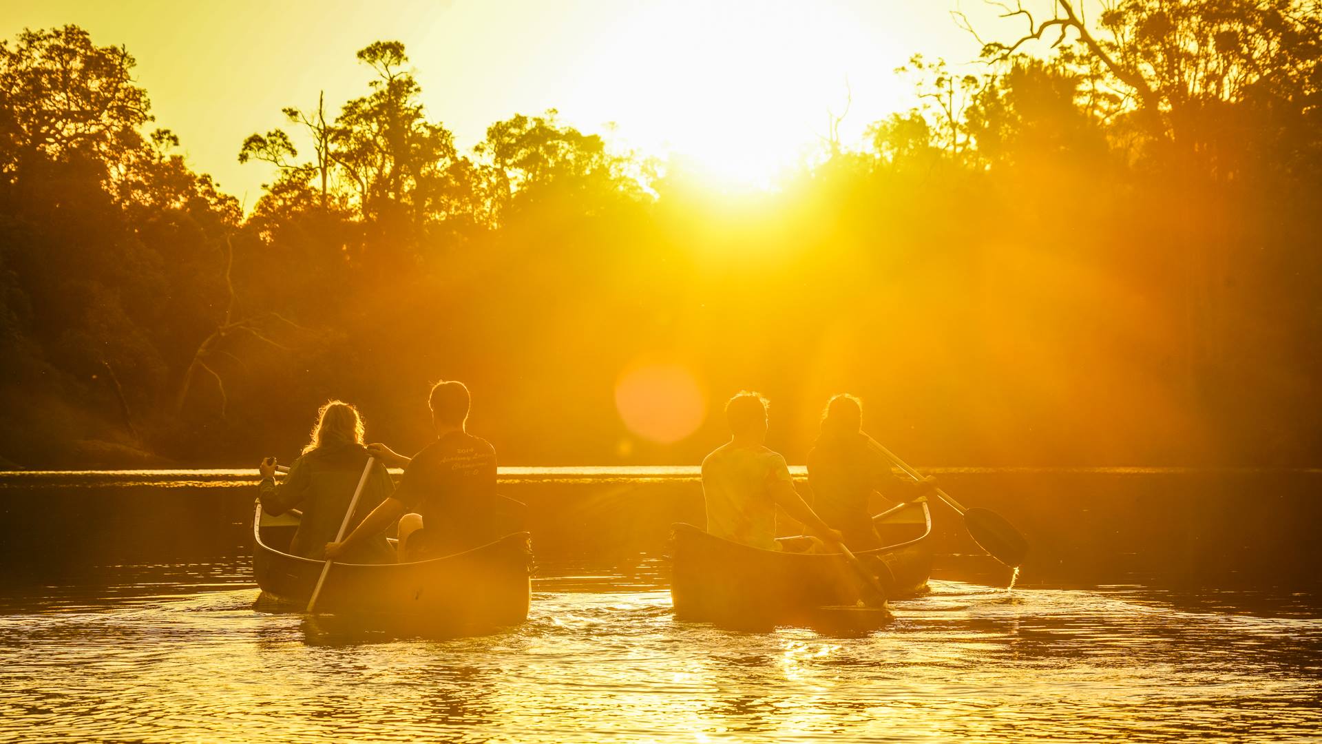 Sunrise shining over people paddling canoes on the Margaret River