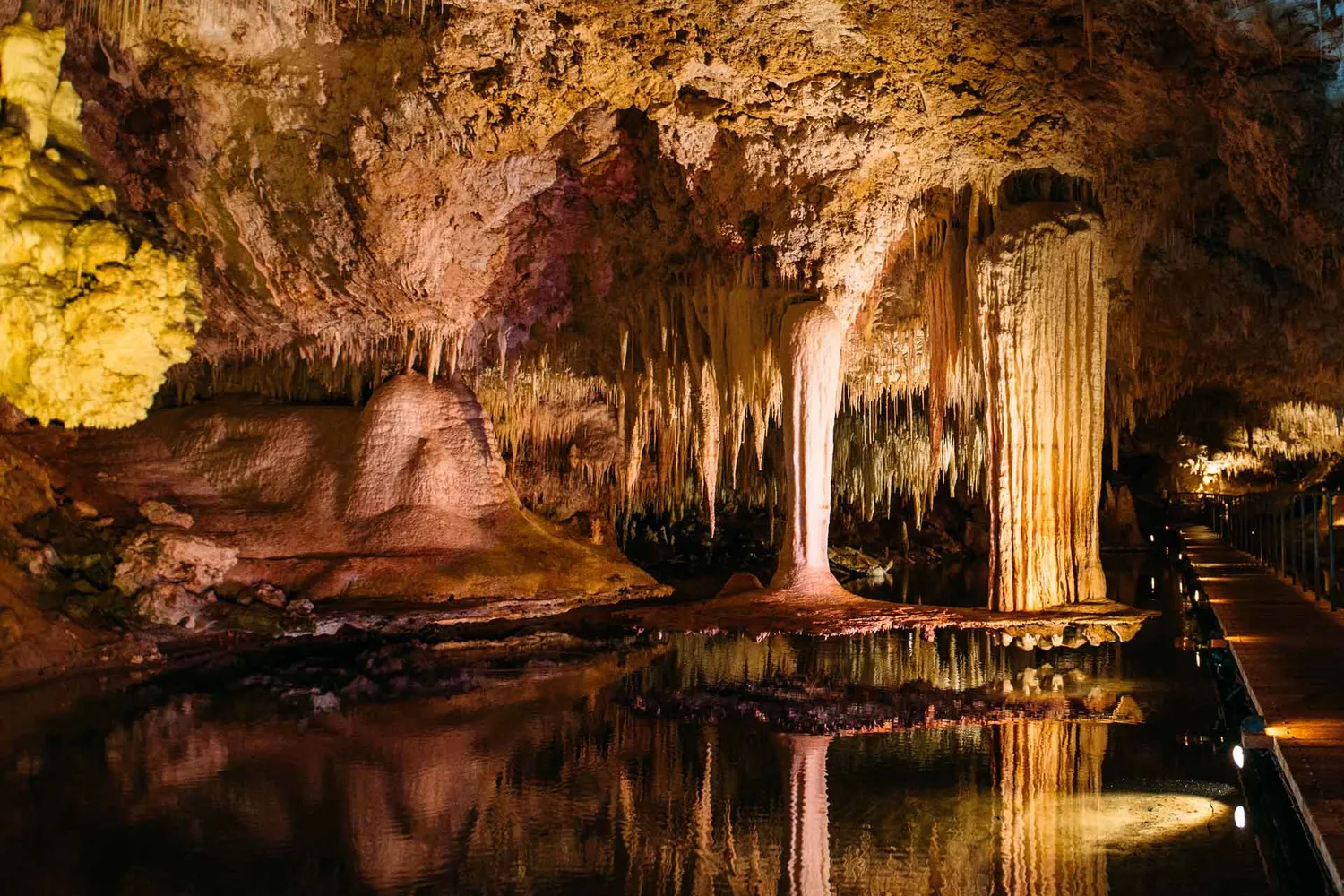 Magical lighting glistens over the water illuminating the enormous stalactites hanging from the roof of Lake Cave, Margaret River.