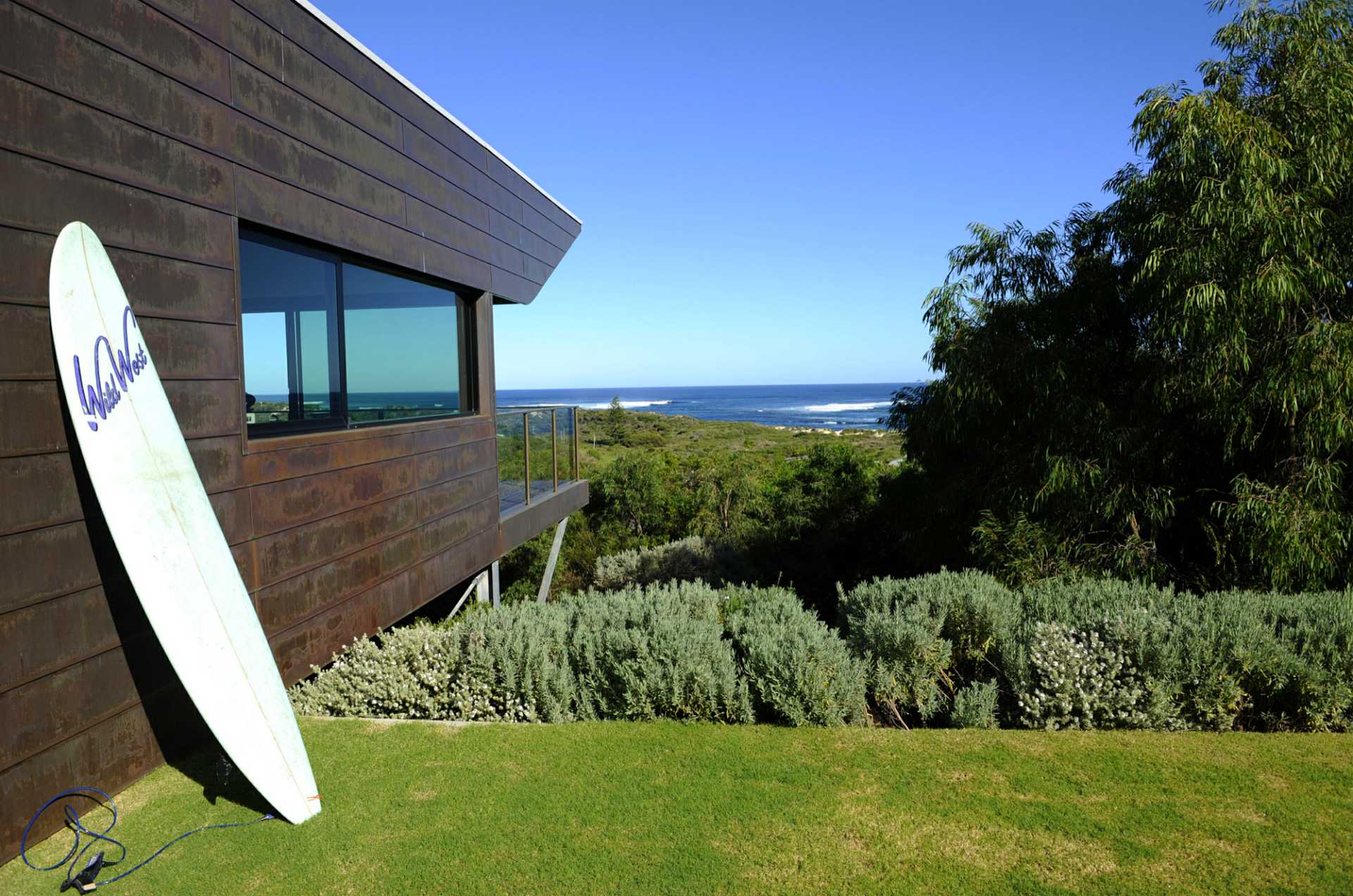 Surfboard leaning up against outside wall of beach house with views of the bombie surf break.